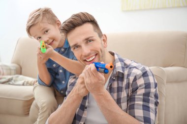 Sevimli çocuk ve babası evde oyuncak silahlarla oynayan