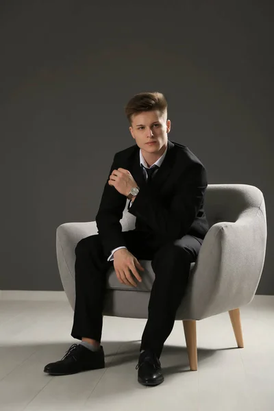 Hombre guapo en traje formal sentado contra la pared gris —  Fotos de Stock