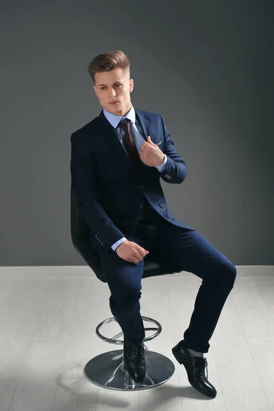 Stilig man i formella kostymen sitter på stol mot grå vägg — Stockfoto