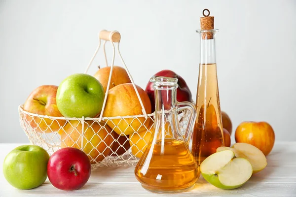 Lasipullo, kannu omenaviinietikkaa ja kori täynnä tuoreita hedelmiä pöydällä — kuvapankkivalokuva
