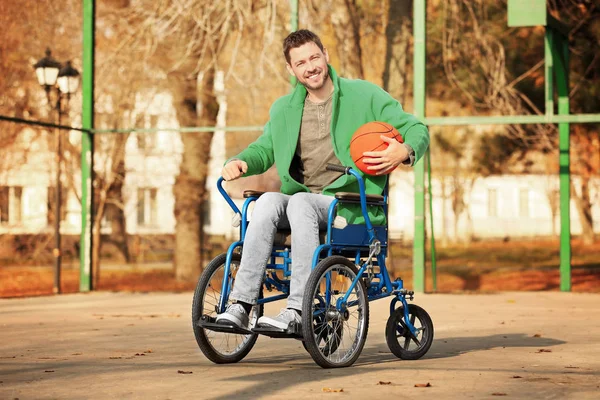 Jovem em cadeira de rodas com bola no playground — Fotografia de Stock
