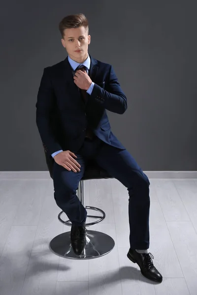 Hombre guapo en traje formal sentado en silla contra la pared gris —  Fotos de Stock