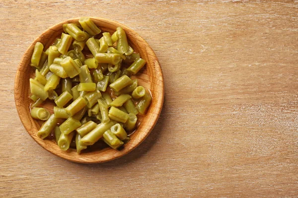 Plate with canned green beans on wooden background