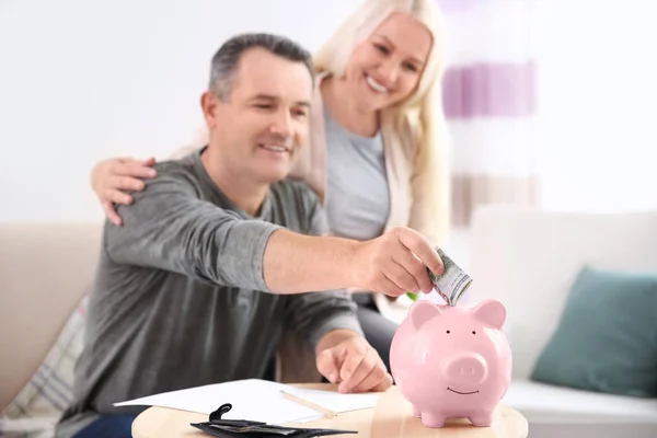 Äldre par sätta pengar i spargrisen hemma — Stockfoto