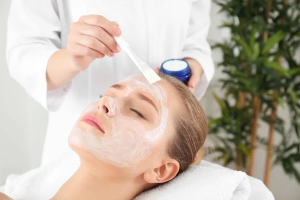 Beautician memasang topeng ke wajah wanita muda di salon spa — Stok Foto