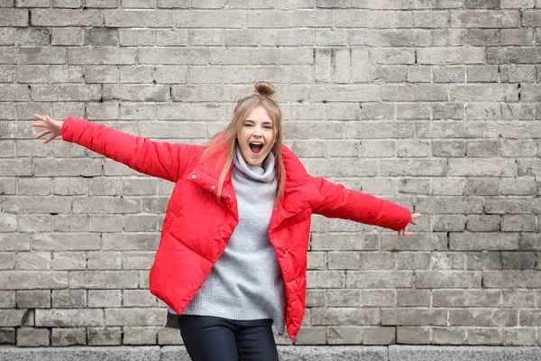 Atractiva chica hipster en chaqueta roja cerca de la pared de ladrillo al aire libre —  Fotos de Stock