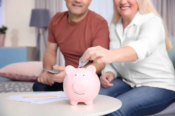 Älteres Ehepaar legt zu Hause Geld in Sparschwein — Stockfoto