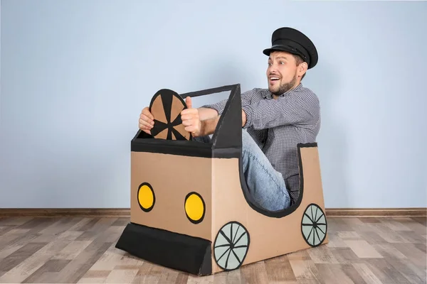 Young man dreaming of buying own auto while playing with cardboard car indoors — Stock Photo, Image