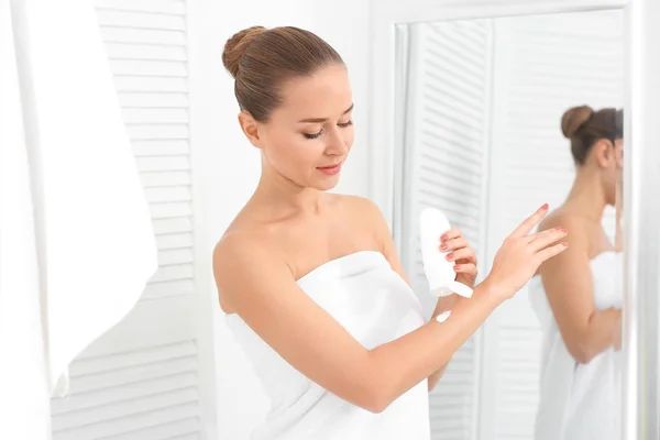 Mujer joven aplicando crema corporal en el baño — Foto de Stock