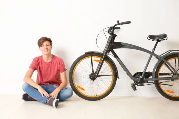 Hipster teenager with bicycle near light wall