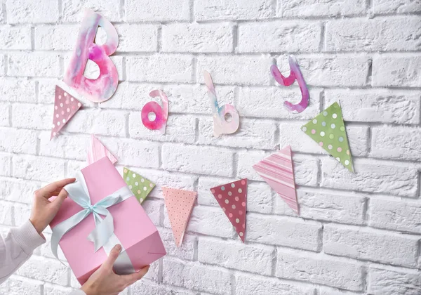 Kobieta, przytrzymanie pudełko na baby shower strony w pobliżu zdobione ściany wewnątrz — Zdjęcie stockowe