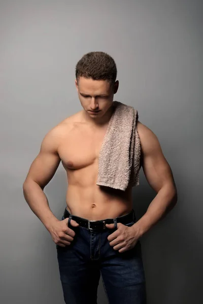 Muscular young bodybuilder with towel on grey background