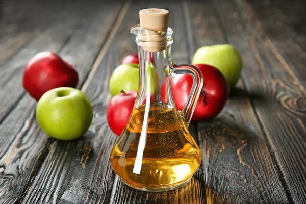 Glaskanna med äppelvinäger och färsk frukt på bordet — Stockfoto