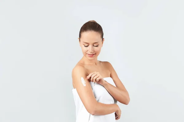 Mulher jovem aplicando creme de corpo no fundo claro — Fotografia de Stock