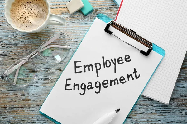 Clipboard and paper with text EMPLOYEE ENGAGEMENT on wooden table