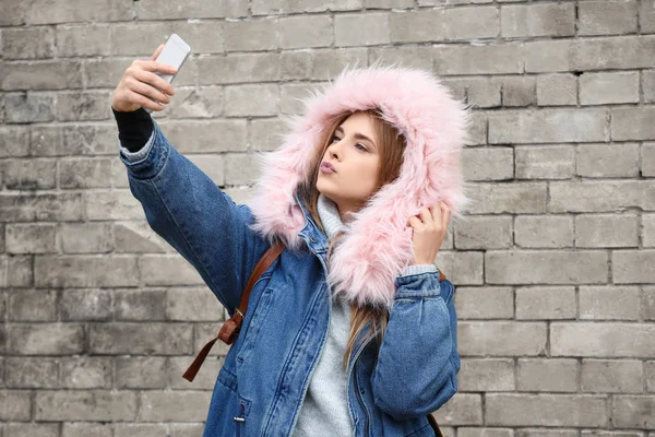 Atractiva chica hipster tomando selfie cerca de la pared de ladrillo al aire libre —  Fotos de Stock