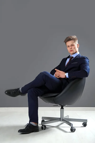 Hombre guapo en traje formal sentado en silla contra la pared gris —  Fotos de Stock