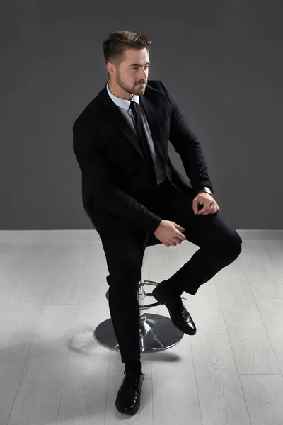 Schöner Mann im formellen Anzug sitzt auf Stuhl gegen graue Wand — Stockfoto