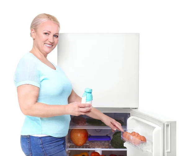 Mature woman with yogurt near refrigerator on white background — Stock Photo, Image