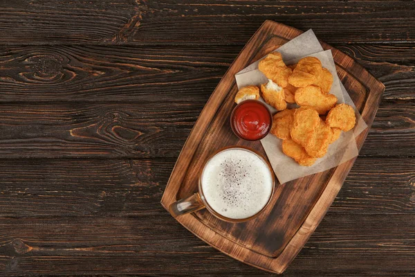 Wooden board with tasty chicken nuggets, beer and sauce on table — Stock Photo, Image
