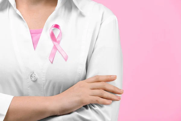 Médico con cinta rosa en la bata contra el fondo de color. Concepto de conciencia sobre el cáncer de mama — Foto de Stock
