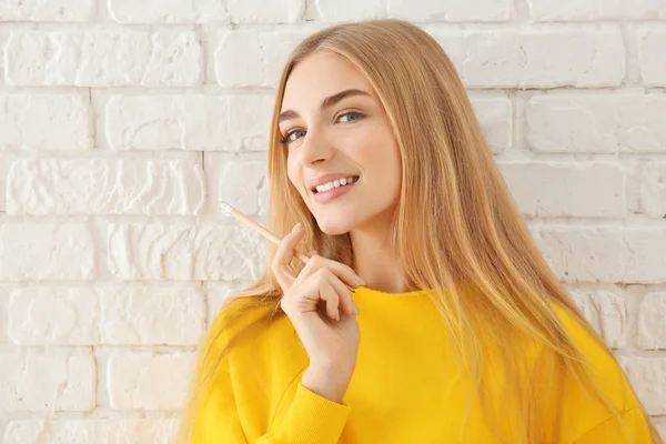 レンガ壁の背景に黄色のトレーナーで笑顔の女性 — ストック写真