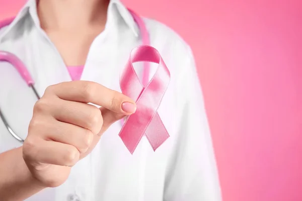 Doctor holding pink ribbon on color background. Breast cancer awareness concept — Stock Photo, Image