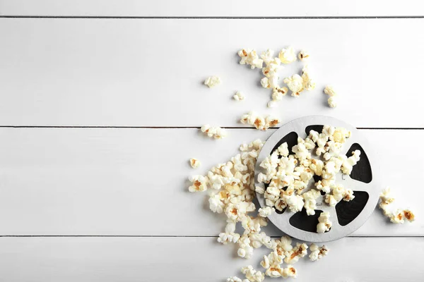 Tasty popcorn and movie reel on white wooden background