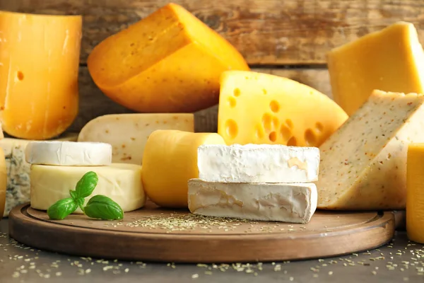 テーブルの上のおいしいチーズの種類と木の板 — ストック写真