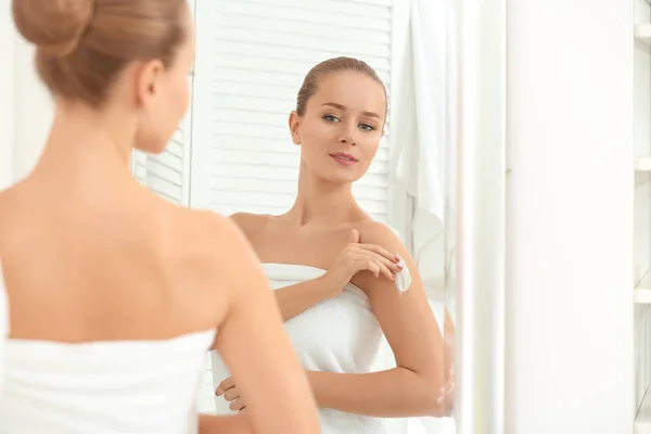 Mujer joven aplicando crema corporal en el baño — Foto de Stock
