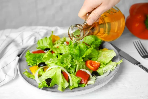 Woman adding tasty apple vinegar into salad with vegetables on plate — Stock Photo, Image