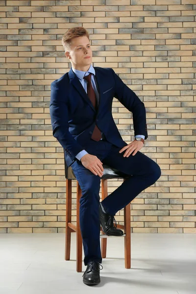 Stilig man i formella kostymen sitter på stol mot tegelvägg — Stockfoto