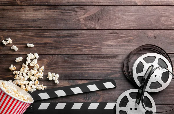 Tasty popcorn, movie reel and clapboard on wooden background