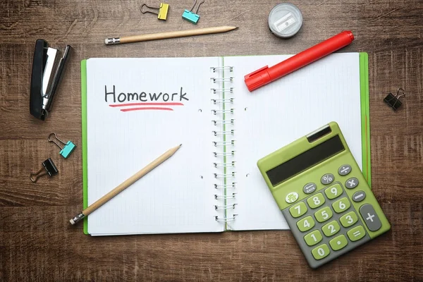 Cuaderno con palabra "Homework" y papelería sobre fondo de madera, vista superior —  Fotos de Stock