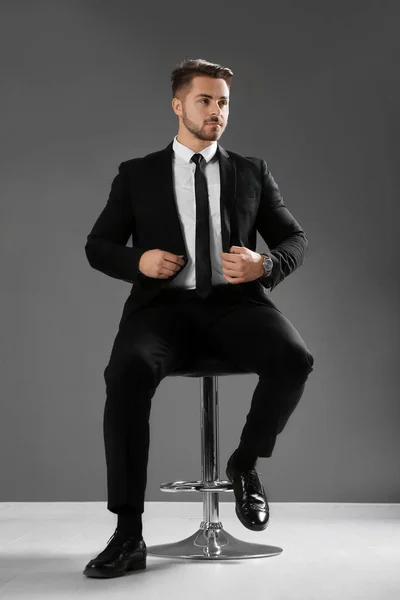 Hombre guapo en traje formal sentado en silla contra la pared gris —  Fotos de Stock