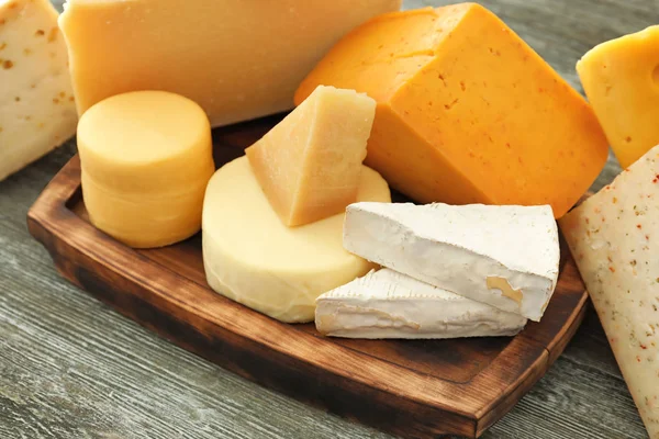 Placa de madeira com diferentes tipos de delicioso queijo na mesa — Fotografia de Stock