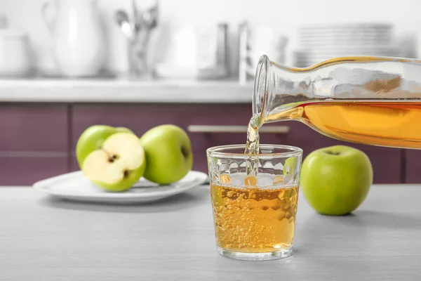 Despejar suco de maçã de garrafa em vidro na mesa da cozinha — Fotografia de Stock