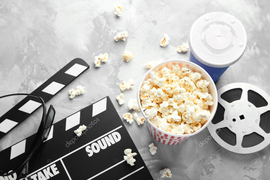 Tasty popcorn, movie reel and clapboard on grey background