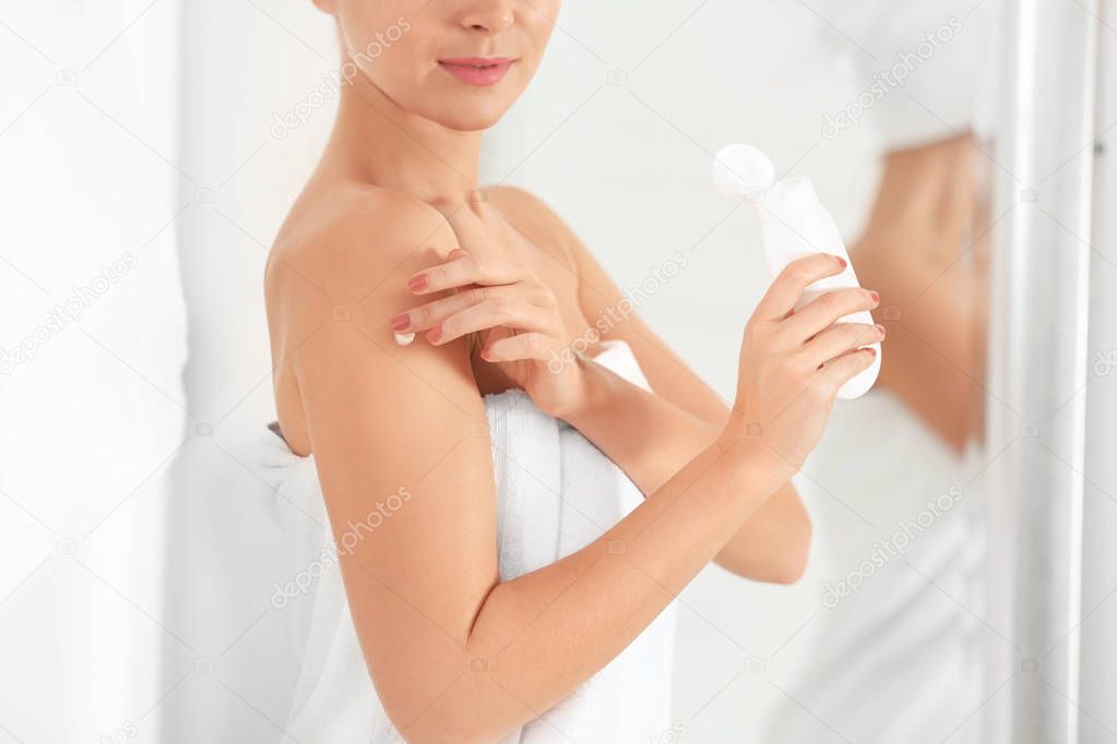 Young woman applying body cream in bathroom, closeup