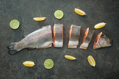 Ham Gökkuşağı alabalığı, limon ve kireç gri arka planda, üstten görünüm kompozisyon