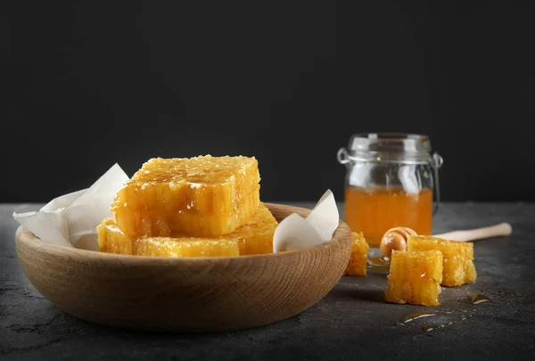 Cuenco con panales dulces y tarro con miel sobre la mesa sobre fondo negro — Foto de Stock