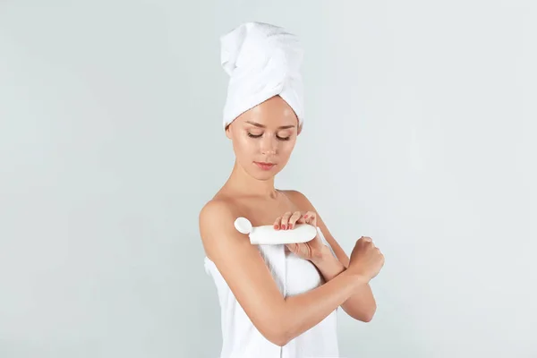 Mujer joven aplicando crema corporal sobre fondo claro — Foto de Stock