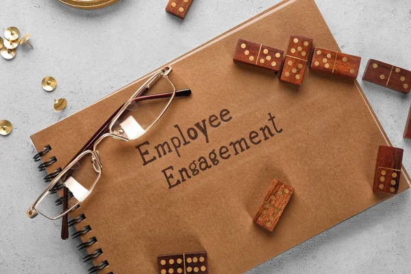 Notepad with text EMPLOYEE ENGAGEMENT, eyeglasses and dominoes on table