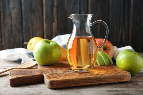 Glaskanna med äppelvinäger och färsk frukt på bordet — Stockfoto