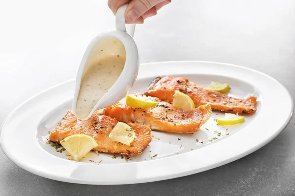 Pouring sauce onto tasty rainbow trout fillets on plate — Stock Photo, Image