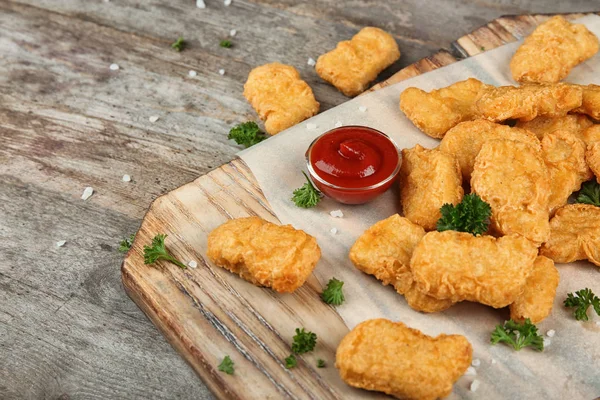 Wooden board with tasty chicken nuggets and sauce on table — Stock Photo, Image