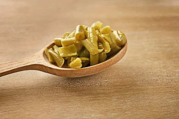 Spoon with canned green beans on wooden background