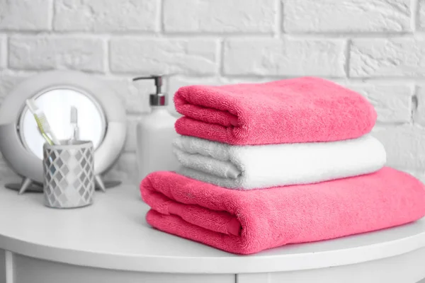 Bunten med rena handdukar och toalettartiklar på bordet nära vit tegelvägg — Stockfoto