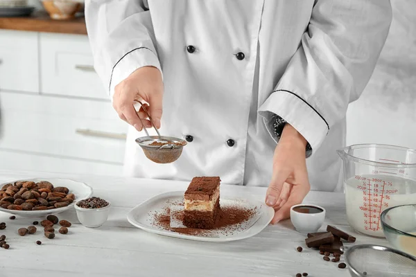 Female chef decorating tasty chocolate cake in kitchen