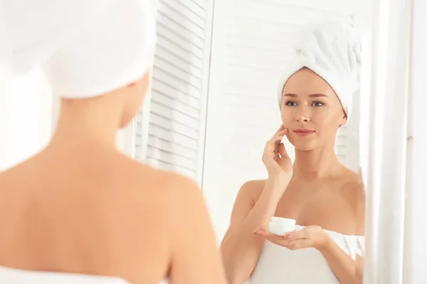 Giovane donna che applica la crema viso in bagno — Foto Stock